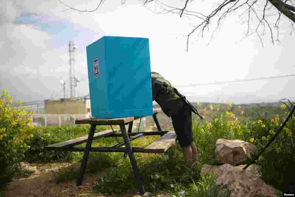 An Israeli soldier casts his ballot for the parliamentary election behind a mobile voting booth in the West Bank Jewish settlement of Migdalim, near Ariel.