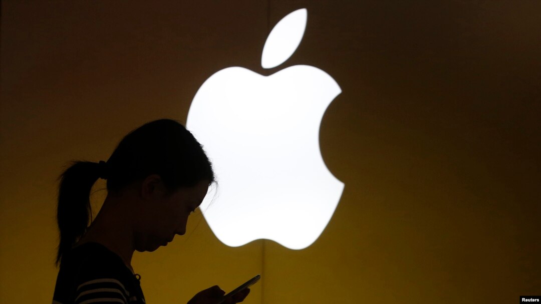 FILE - A woman looks at the screen of her mobile phone in front of an Apple store in Shanghai, China.