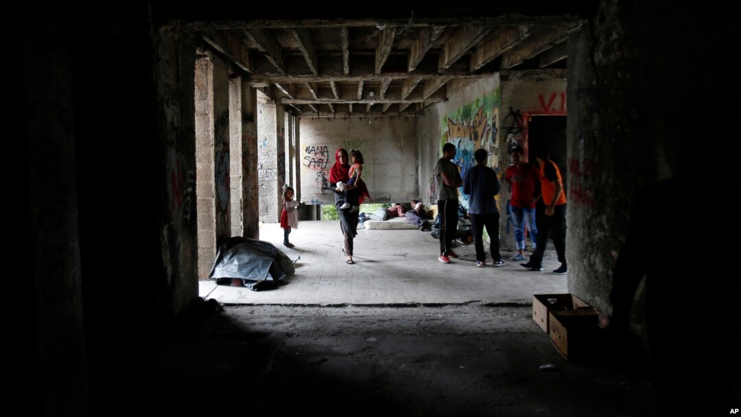 FILE - A migrant woman walks with her baby in a makeshift migrant camp in Bihac, 450 kms northwest of Sarajevo, Bosnia, Aug. 14, 2018. 